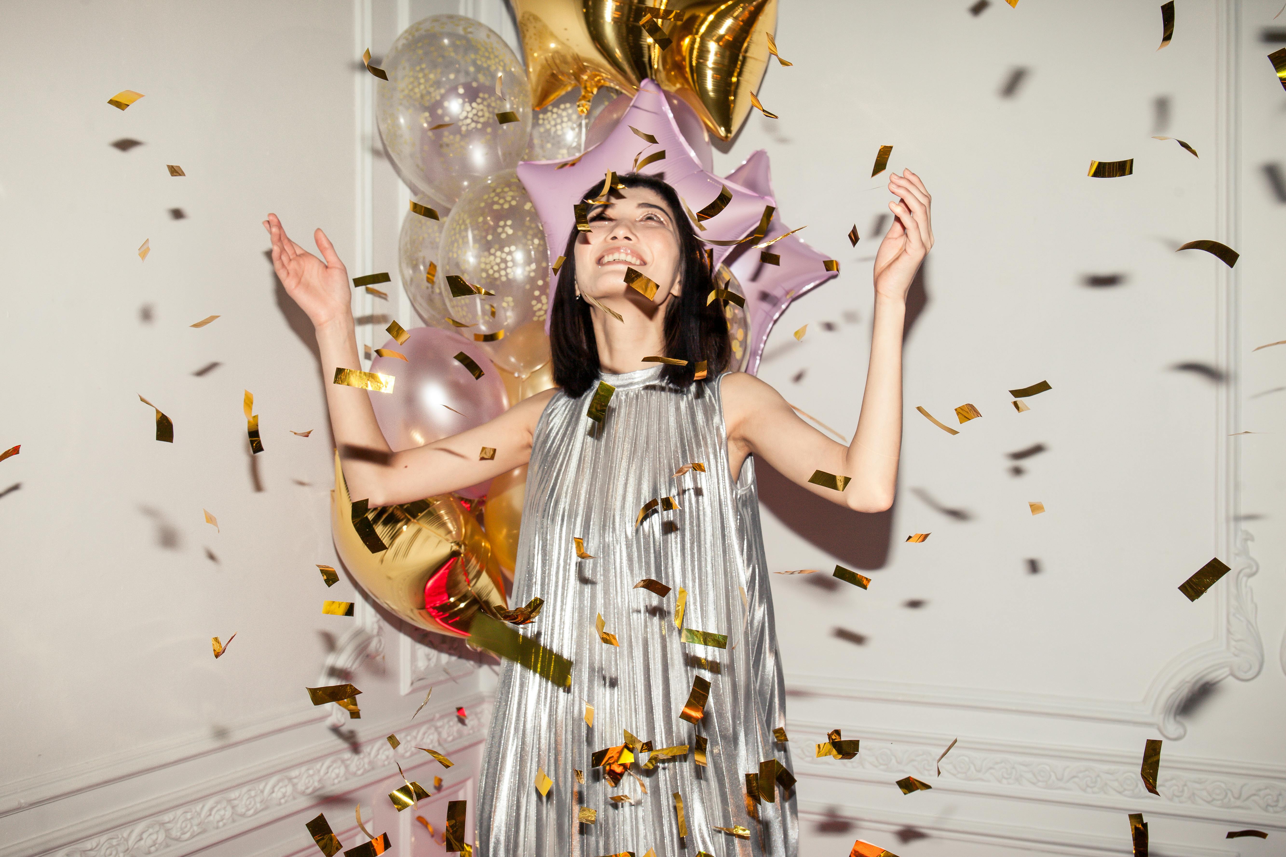 Joyous indoor celebration with balloons and confetti featuring a stylish young woman.